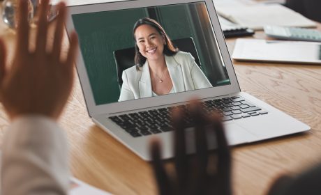 Colleagues waving to each other through a laptop screen as part of an online meeting.