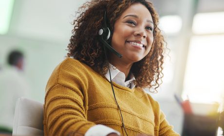 A smiling woman in a yellow sweater listening on her earphones.