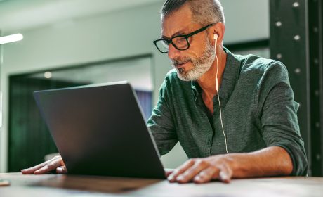 A man looking at his laptop and listening on his earphones.