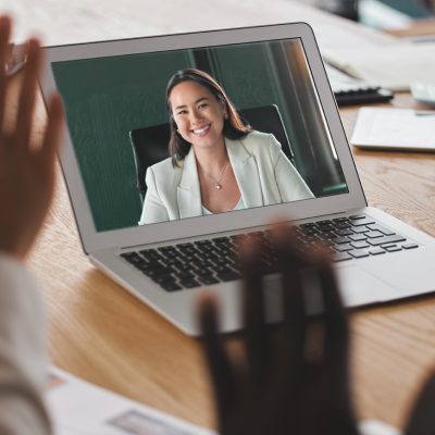 Colleagues waving to each other through a laptop screen as part of an online meeting.