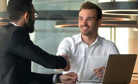 Two men shaking hands in front of a laptop