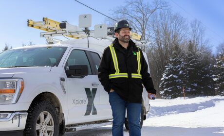 A network technician standing in a snowy forested area with his Xplore branded truck in the background.