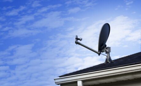 A satellite dish on the corner of a roof, blue sky in the background.