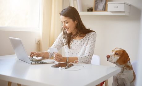 Woman sitting down in front of a laptop with a dog by her side