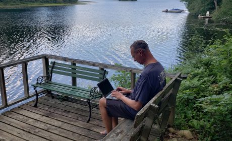Man working on fibre-connected laptop on the deck of his rural Quebec cottage - which overlooks a beautiful lake.