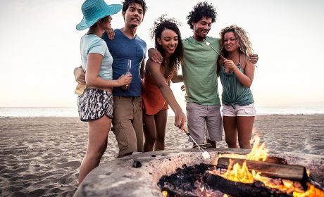 Group of friends at the beach in front of a fire pit melting a marshmallow