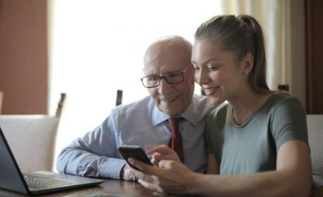 Young woman on her cellphone with her grandfather in front of a laptop