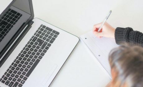 Person writing on paper whilst looking at a laptop