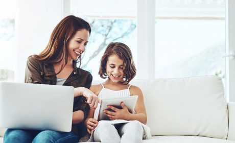 Mother on her laptop & daughter on a table both sitting on the sofa