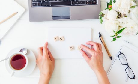 A person sitting in front of their laptop with a cup of coffee spelling out "To-Do" on white card