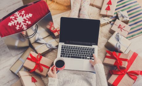 Une image d'un individu se servant d'un ordinateur portable, entouré de cadeaux du temps des fêtes.