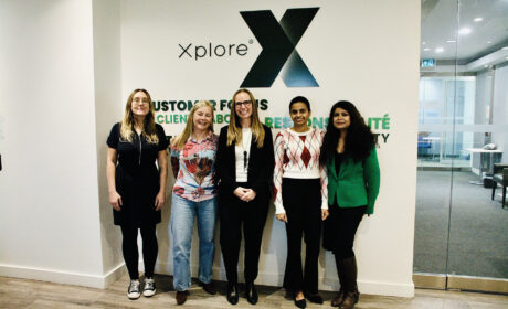 Xplore's Women's History Month panel organizers and contributors standing together in front of an Xplore branded wall.