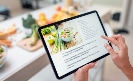 A person scrolling through a recipe on their tablet with their counter full of veggies and other ingredients in the background