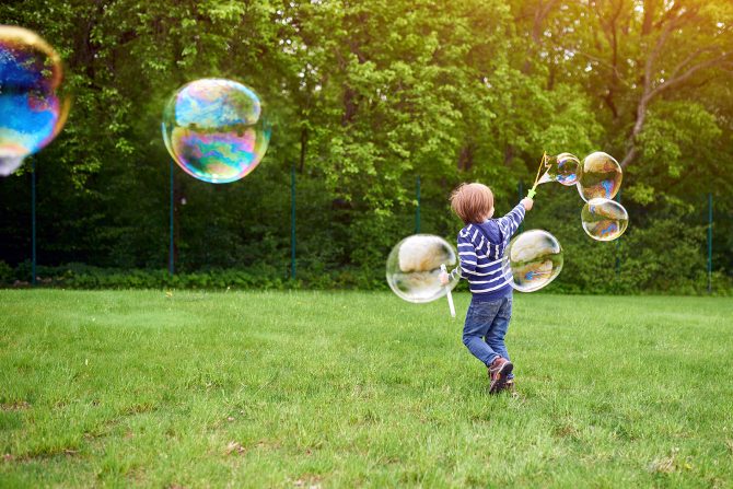 A boy chasing bubbles in the grass