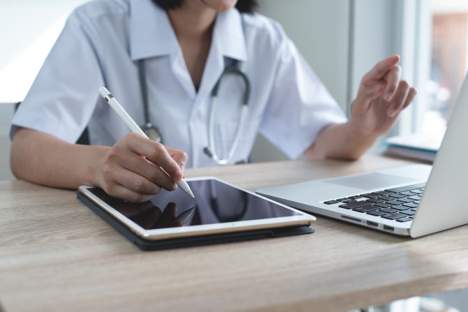 A medical professional using a tablet and laptop with fast internet