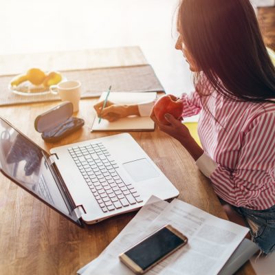 Woman making notes in front of a laptop