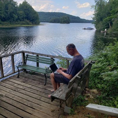 Man working on fibre-connected laptop on the deck of his rural Quebec cottage - which overlooks a beautiful lake.