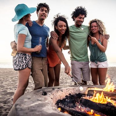 Group of friends at the beach in front of a fire pit melting a marshmallow