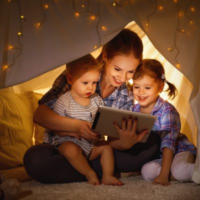 Mother with her to children using a tablet whilst sitting under a blanket fort