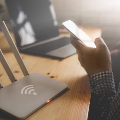 Person holding a cellphone sitting in front of a Wi-Fi modem