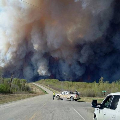 Cars pulled over to the side of the road with plumes of smoke in the distance