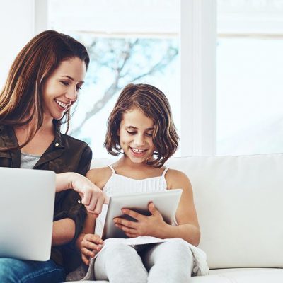 Mother on her laptop & daughter on a internet connected tablet both sitting on the sofa