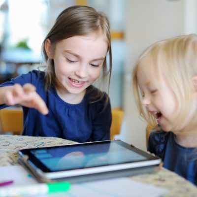 Two girls playing on a internet connected tablet at the table