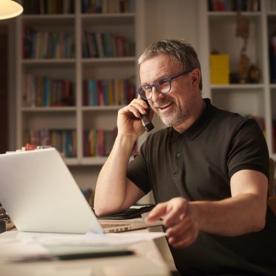 Une personne parlant sur son téléphone résidentiel, assis devant un ordinateur portable.