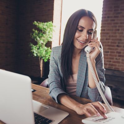 Woman using a home phone sitting in front of laptop