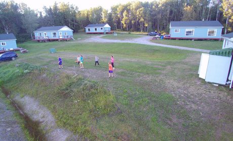 A photo of children playing in on a field in Rufus Lake, with a number of cottages in the background.