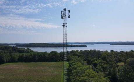 A cell tower overlooking a landscape of trees and a body of water