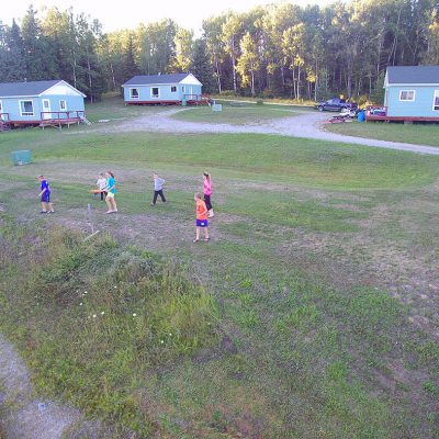 A photo of children playing in on a field in Rufus Lake, with a number of cottages in the background.